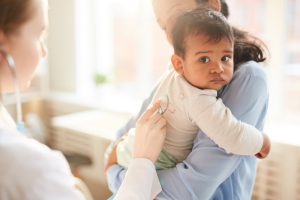 Doctor examining the child Mother holding her baby to her chest while female doctor examining him with stethoscope at hospital